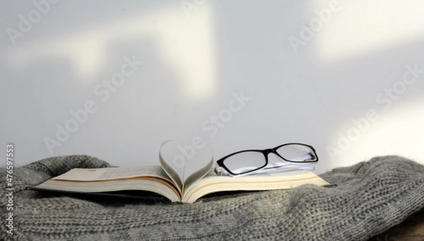 Obraz The pages of an open book are folded in the shape of a heart. The book is on the sweater. There are glasses on the book. Concept education