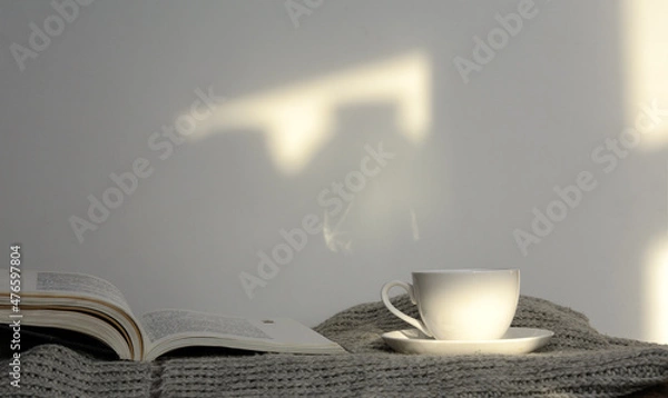 Obraz An open book lies on a knitted sweater. Next to a cup of coffee. White background. Concept - morning coffee