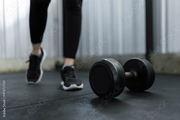 Fototapeta exercise concept The black rubber coated round dumbbell lying on the gym ground in front of the person who wears black trainers