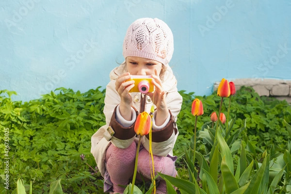Fototapeta a girl in a white jacket sits with a small camera in front of a tulip