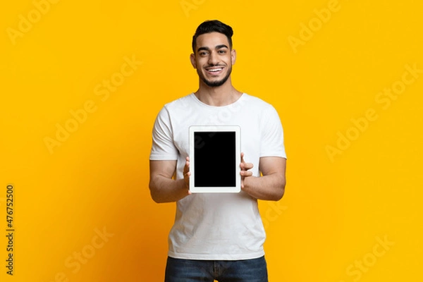 Fototapeta Cheerful arab guy showing digital tablet with blank screen