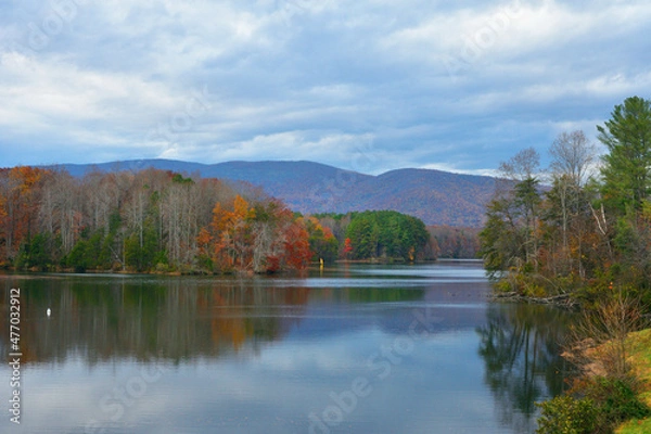 Obraz A windsurfer navigates on a pristine mountain lake with colorful clouds and autumnal colors in the trees.