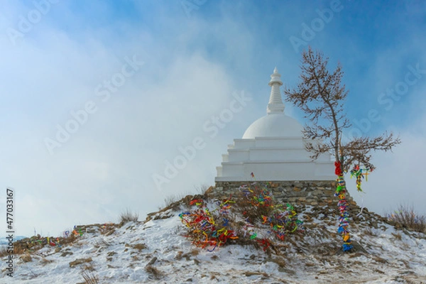 Fototapeta White Buddhist stupa and ritual trees with colorful ribbons on a cloudy winter day at the top of the sacred island of Ogoy. Lake Baikal, Siberia, Russia