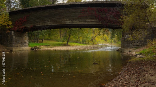Obraz Autumn color reflects of the water beneath a wooden covered bridge in rural Virginia
