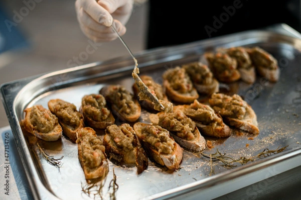 Fototapeta hand of chef spreads by spoon the vegetable blend on slices of baguette on tray