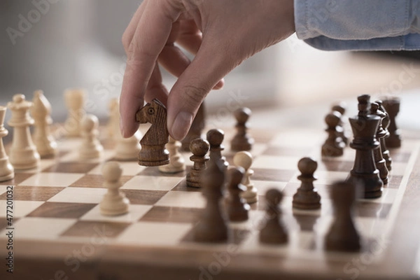 Fototapeta Chess game in action. The player a young girl performs a move of a chess piece horse figure for a game of chess horse soars in the air. Wooden brown checkerboard.
