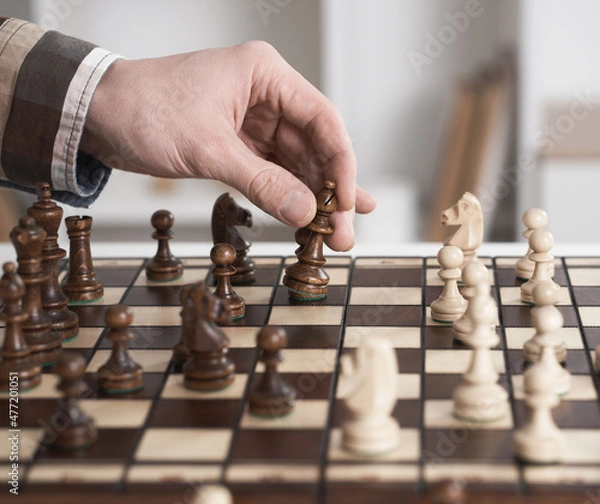 Fototapeta Chess game. The player in the shirt makes a move. Hand-sleeved shirt in a cage take on a wooden figure. Execution of a move with the right hand. Chess piece ferz officer.
