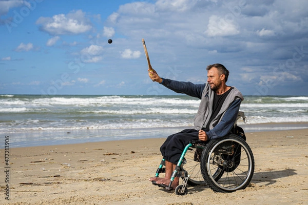 Fototapeta Disabled man sitting on a wheelchair playing paddle ball on the beach