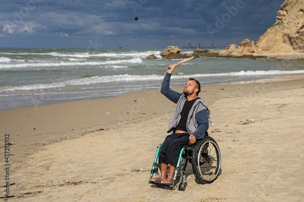 Obraz Disabled man sitting on a wheelchair playing paddle ball on the beach