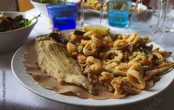 Obraz White dish with fried fish and vegetables on the restaurant table.