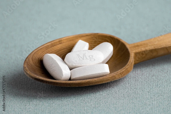 Fototapeta Tablets , vitamins with the abbreviation Mg ( magnesia, the macronutrient magnesium ) lying in a wooden spoon on a light background. Copy space.
