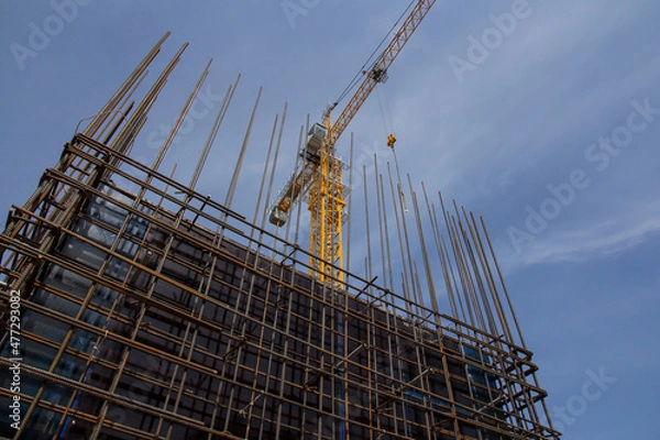Fototapeta Reinforced concrete structure and tower crane against the blue sky. Foundation construction. Construction site concrete structure.