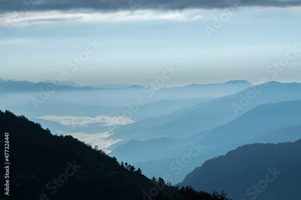 Fototapeta Sunrise scene as seen from Okhrey, Sikkim, India. Sun rising from the back of mountain , blue fog in the middleground of the picture.