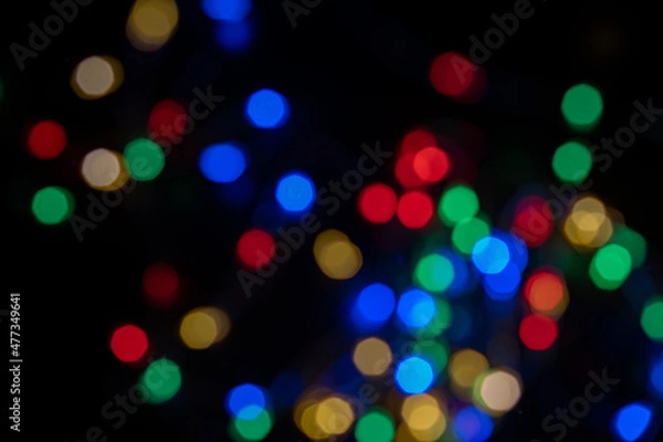 Fototapeta Defocused bokeh lights on black background, an abstract naturally blurred backdrop for Christmas eve or birthday party. Festive light texture. Colorful garland in blur. Overlay effect for design