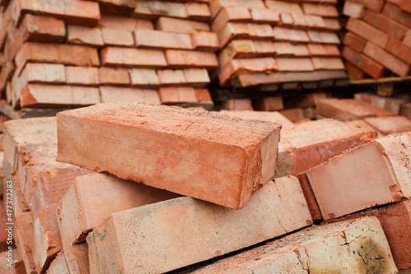 Obraz A stack of red clay bricks in rows close up. Lot of stacks of bricks on construction site