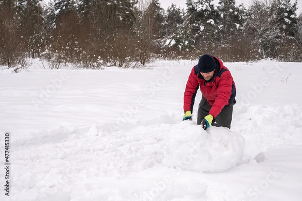 Fototapeta man makes a snowball for a snowman