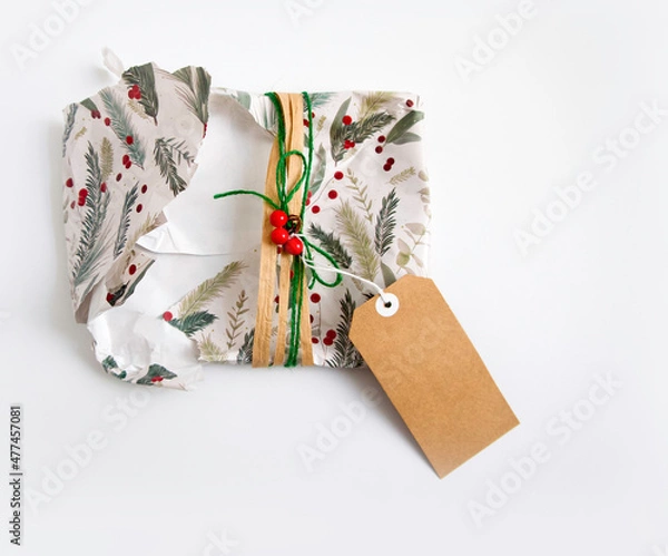 Obraz Torn and empty Christmas wrapping with wrapping paper, twine, ribbon, present topper and a blank gift tag. Copyspace, isolated on white background. Opening Christmas gift or present concept.
