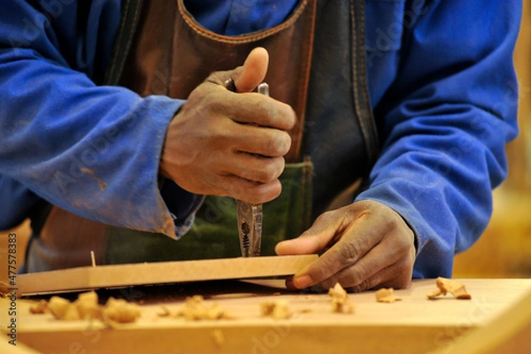 Fototapeta A detailed close up shot of an African male woodworker using pliers to pull out a screw in a piece of wood in a furniture factory, Johannesburg, South Africa