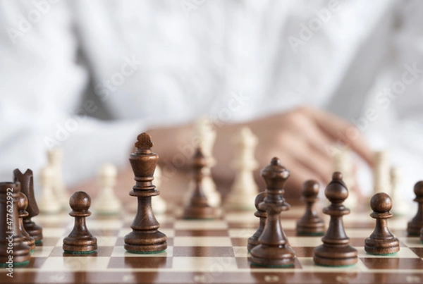 Obraz Chess pieces close up. The chess player sits on the opposite side of the opponent. Chess game. Started drafting a strategy making decisions with quick thinking