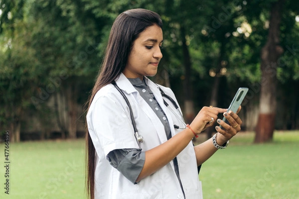Obraz Indian female doctor holding using cell phone. Healthcare telemedicine online remote consultation mobile medical tech application concept