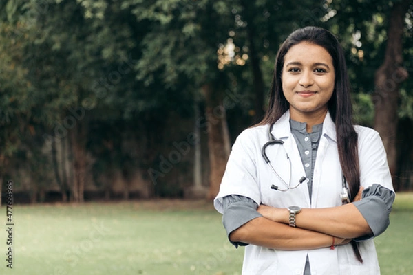 Obraz Portrait of confident Indian doctor wear white coat, standing at outdoors with arms crossed on chest. professional front line covid warriors during covid-19, medical service concept. with copy space