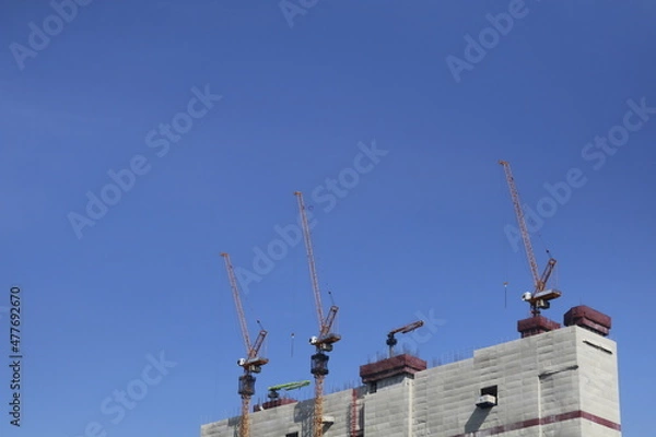 Obraz Cranes build tall buildings in the middle of the city on an empty cloudless day