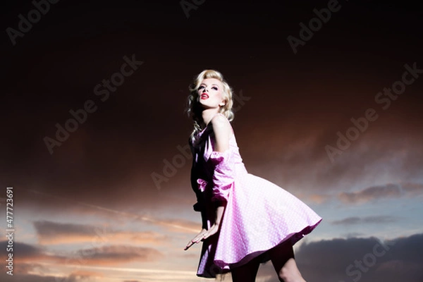 Fototapeta Woman in monroe dress on dramatic sky. Female model in a fashion dress outdoor.