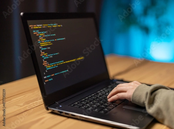 Fototapeta Close up of female hands typing on modern laptop while writing data code. Woman in eyeglasses sitting at home during evening time and working on portable computer.