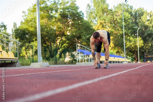 Fototapeta Athletic man with a naked torso practicing stretching exercise before running to the stadium. Healthy lifestyle