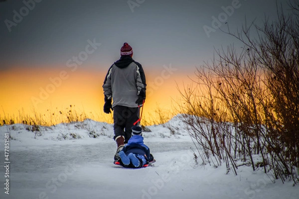 Obraz Winter fun: man is pulling a child on a sled