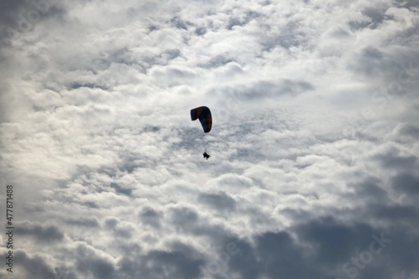 Fototapeta Contours of a paraglider with tourists in the back light in cloudy weather while flying through the sky.
