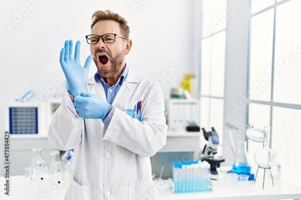 Fototapeta Middle age man working at scientist laboratory angry and mad screaming frustrated and furious, shouting with anger. rage and aggressive concept.