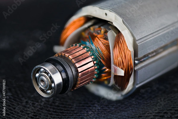 Fototapeta Rotor and stator detail of electric DC motor on black mesh background. Closeup of steel ball bearing, copper commutator or coil wires inside metal laminations of drill machine engine on dark blue net.