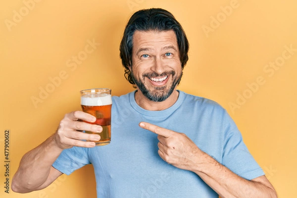 Fototapeta Middle age caucasian man drinking a pint of beer smiling happy pointing with hand and finger