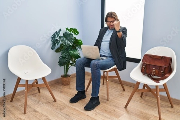 Fototapeta Handsome middle age man sitting at waiting room working with laptop angry and mad raising fist frustrated and furious while shouting with anger. rage and aggressive concept.