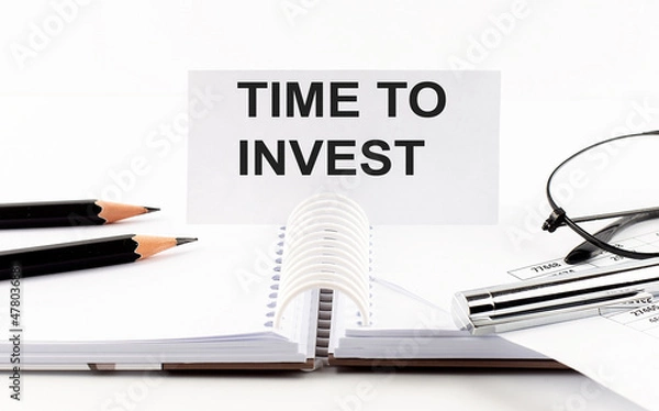 Fototapeta Text TIME TO INVEST on paper card,pen, pencils, glasses,financial documentation on table - business concept