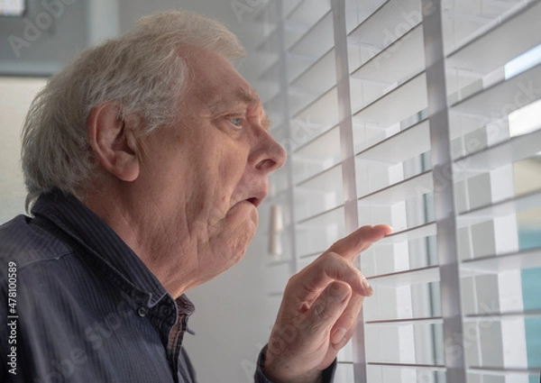 Fototapeta Senior man with funny facial expression looking out of window blinds 