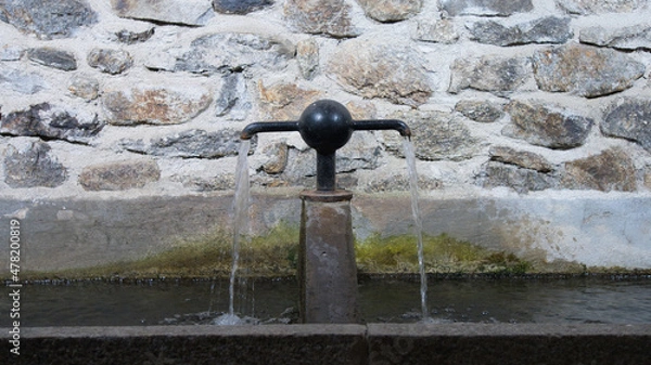 Fototapeta Close up of a metal and stone village fountain, water flowing from the taps in two directions