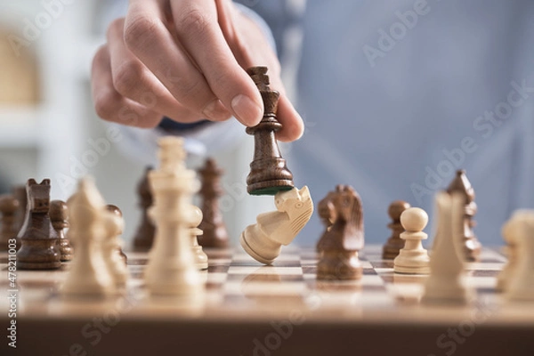 Fototapeta Man's hand holds a chess piece king. A dark colored chess piece. The figure flies. Chess game making a move by a player is an intellectual game.
