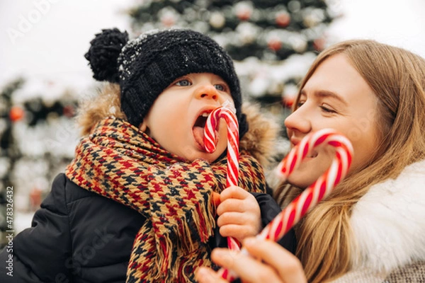 Fototapeta Happy mother and little child with Christmas candies, at the Christmas fair, happy family on the background of the city