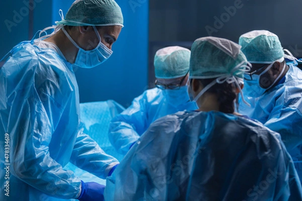 Fototapeta Multiracial team of professional medical surgeons performs the surgical operation in a modern hospital. Doctors are working to save the patient. Medicine, health, cardiology and transplantation.