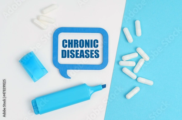Obraz On a white and blue table are pills, a marker and a blue plaque with the inscription - CHRONIC DISEASES