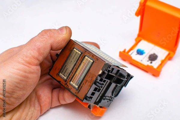 Fototapeta close up, faulty, dirty color ink printhead in the hand of a service center master on a clean white background