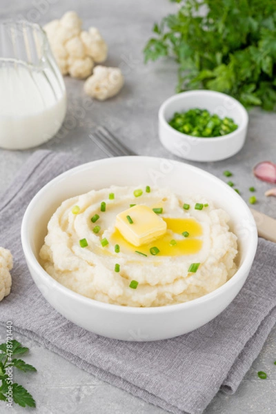 Fototapeta Cauliflower puree with butter and green onions in a white bowl on a gray concrete background. Healthy food. Copy space.
