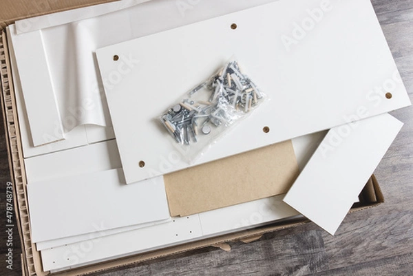 Fototapeta Opened box with furniture assembly parts and tools on the floor. Self assembling furniture at home concept.
