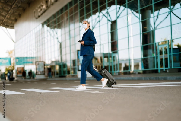 Fototapeta Grey woman in face mask using cellphone while walking on zebra crossing
