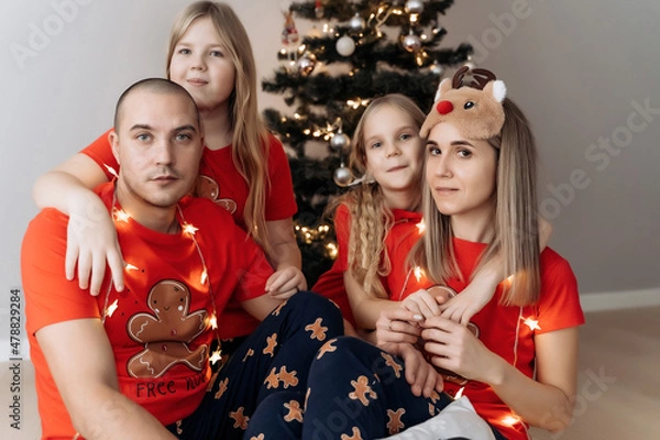 Fototapeta A family in red holiday T-shirts sitting at the Christmas tree and celebrating the New Year