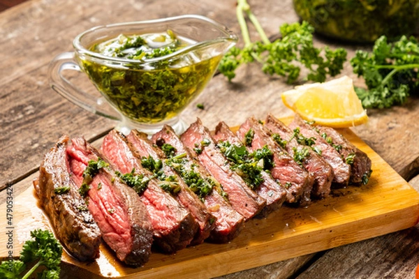 Obraz Appetizing beef steak cooked and sliced on a wooden table with chimichurri sauce.