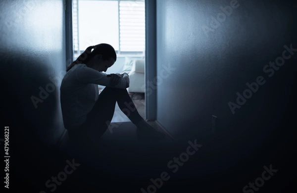 Fototapeta silhouette of a sad woman sitting next to window in a dark room 