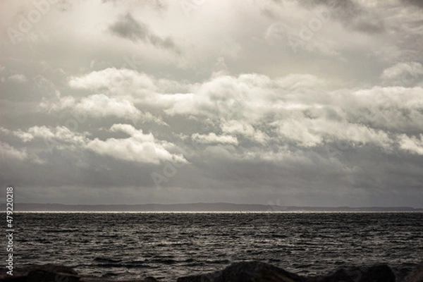 Obraz Sonne durchbricht Wolken am Meer in schwarz-weiß
